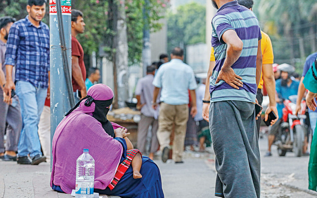 A mother, weary of walking under the sun, rests on the sidewalk with her child on her lap